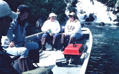 A group of people sit in a boat in front of an icy waterfall.