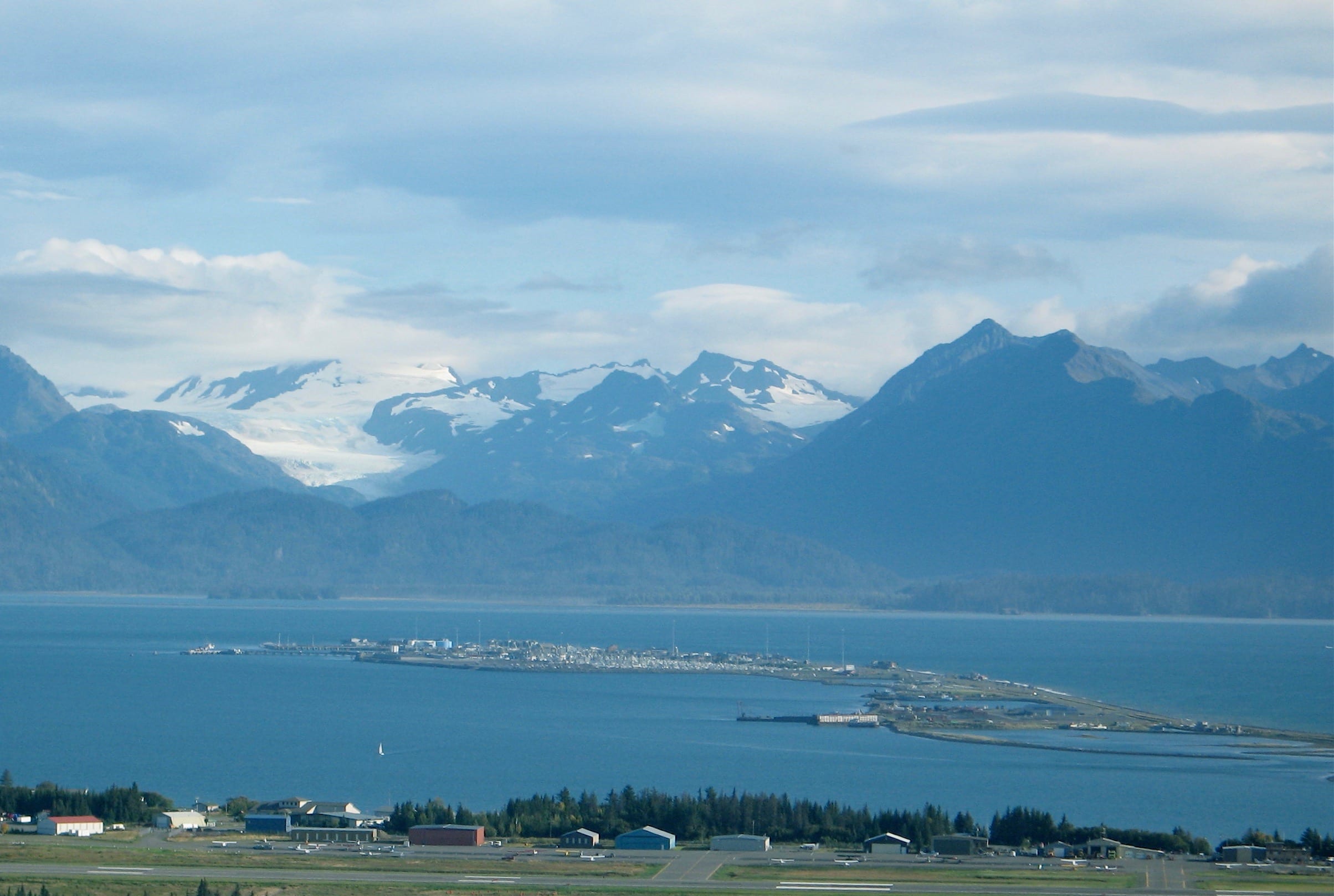 Long windy island in middle of blue water surrounded by mountains