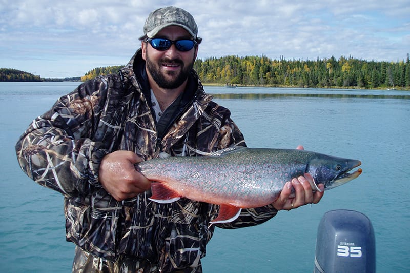A man holds up a large char caught from a motor boat.