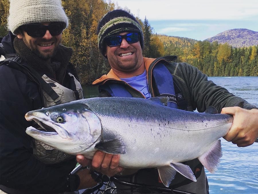 A man holds up a very large salmon out of a clear blue river.