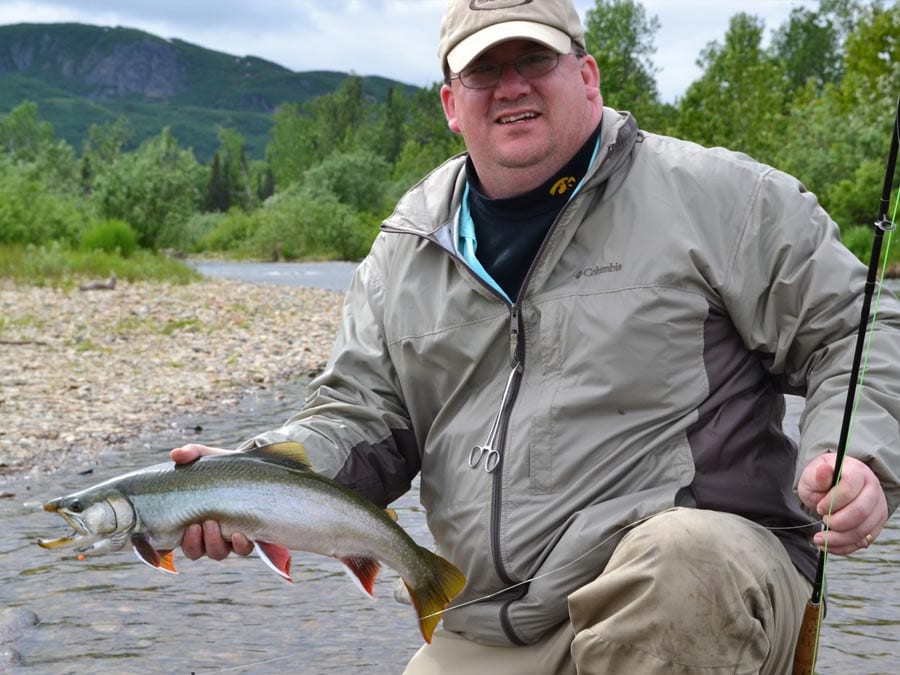 A man holds up a dolly varden caught on a fly rod.