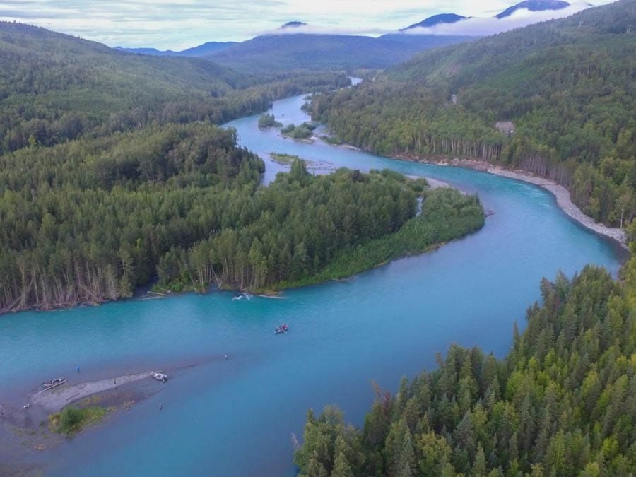 A float boat meanders down a large sweeping mountain river.