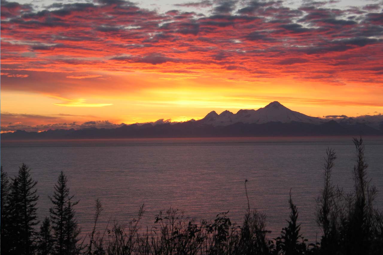 A bright red sunset paints the clouds above a set of high mountain peaks